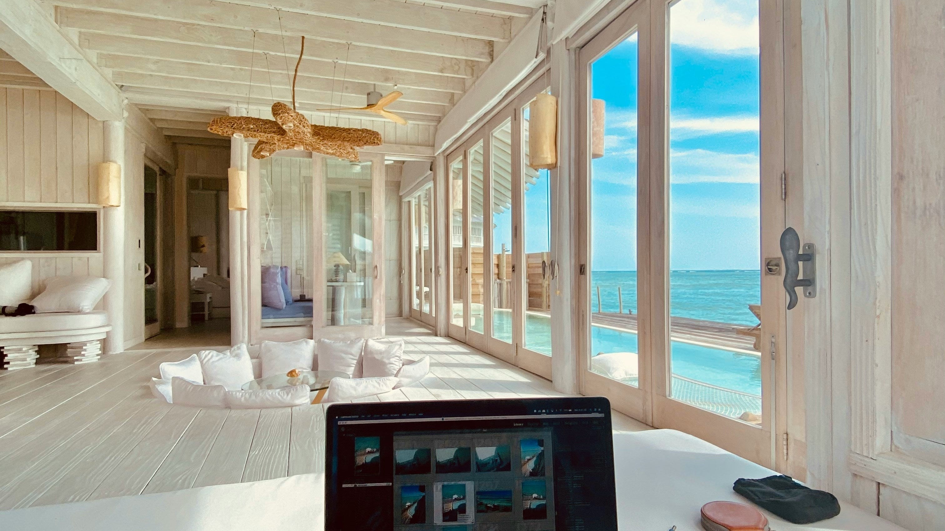 A laptop on a wooden desk in a bright coastal-inspired home office, showcasing natural light, and minimalist home office decorating ideas.