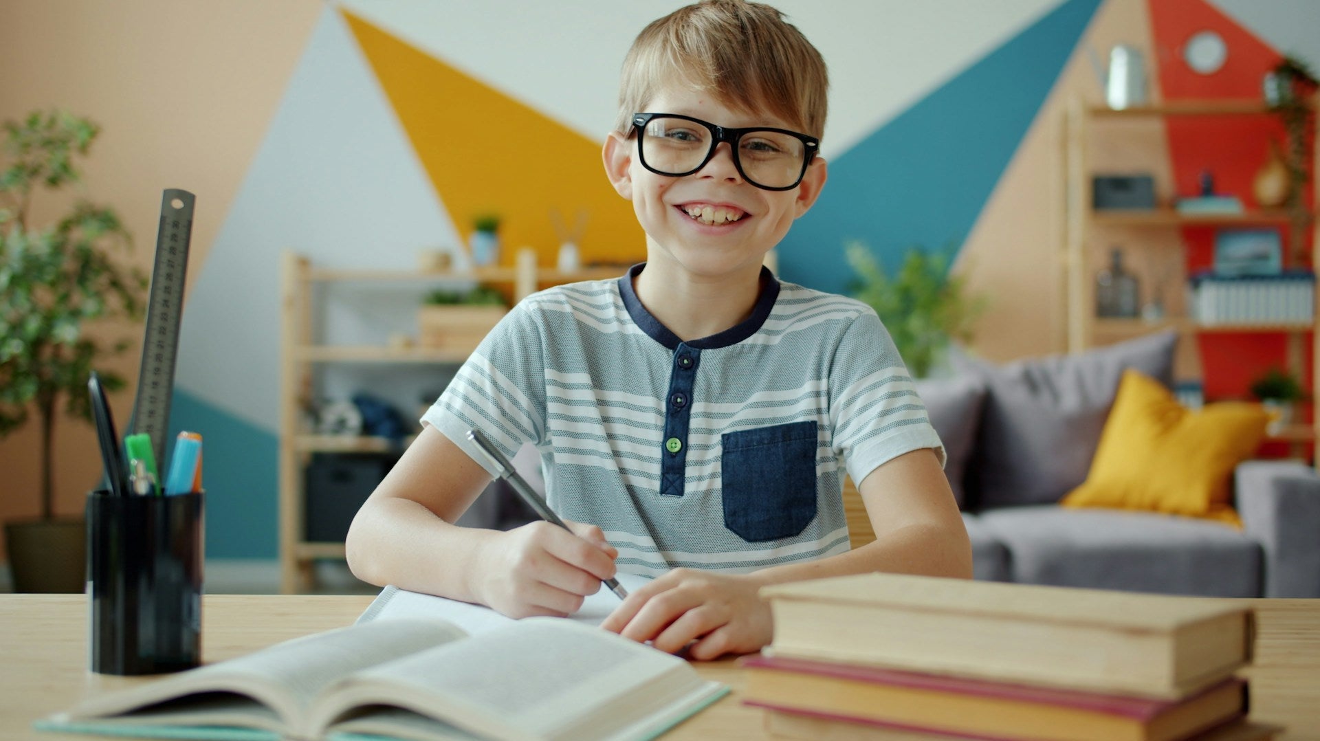 Smiling boy with glasses studying at a desk, showing how proper posture affects focus and learning — does posture affect learning.