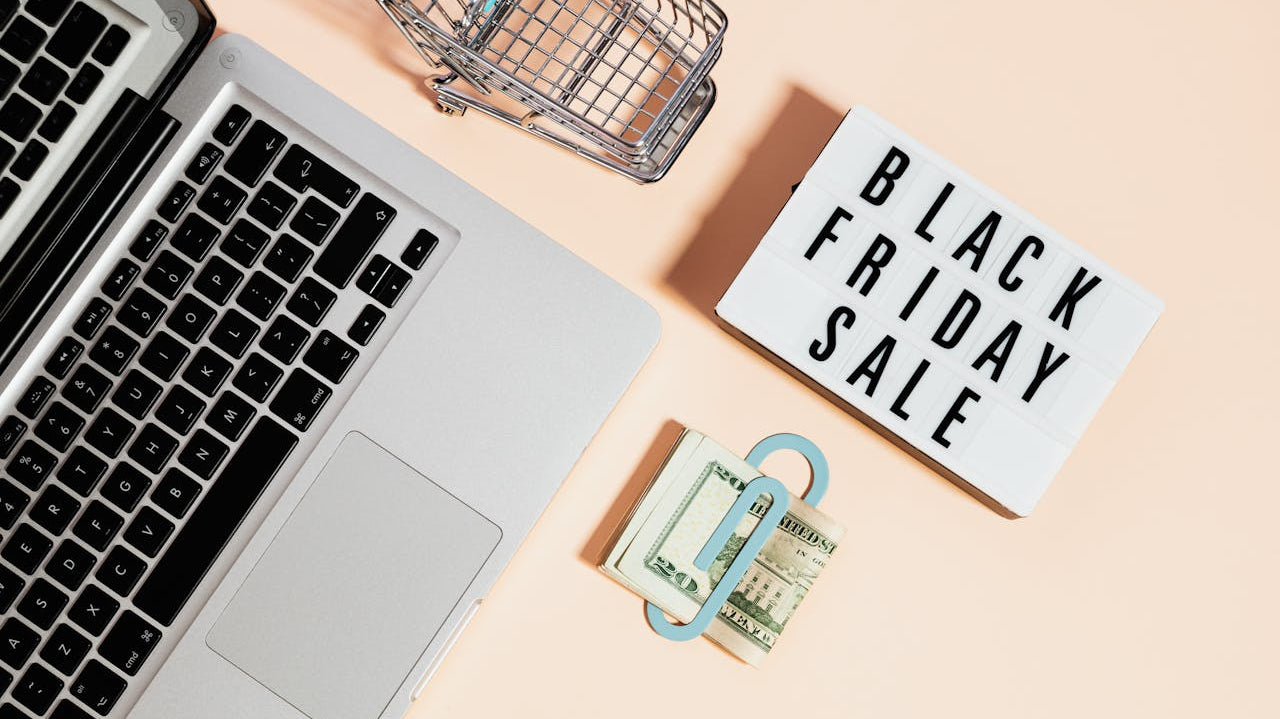 Black Friday sale banner top view featuring a laptop, shopping cart, and an ergonomic chair, highlighting online deals and office furniture discounts.