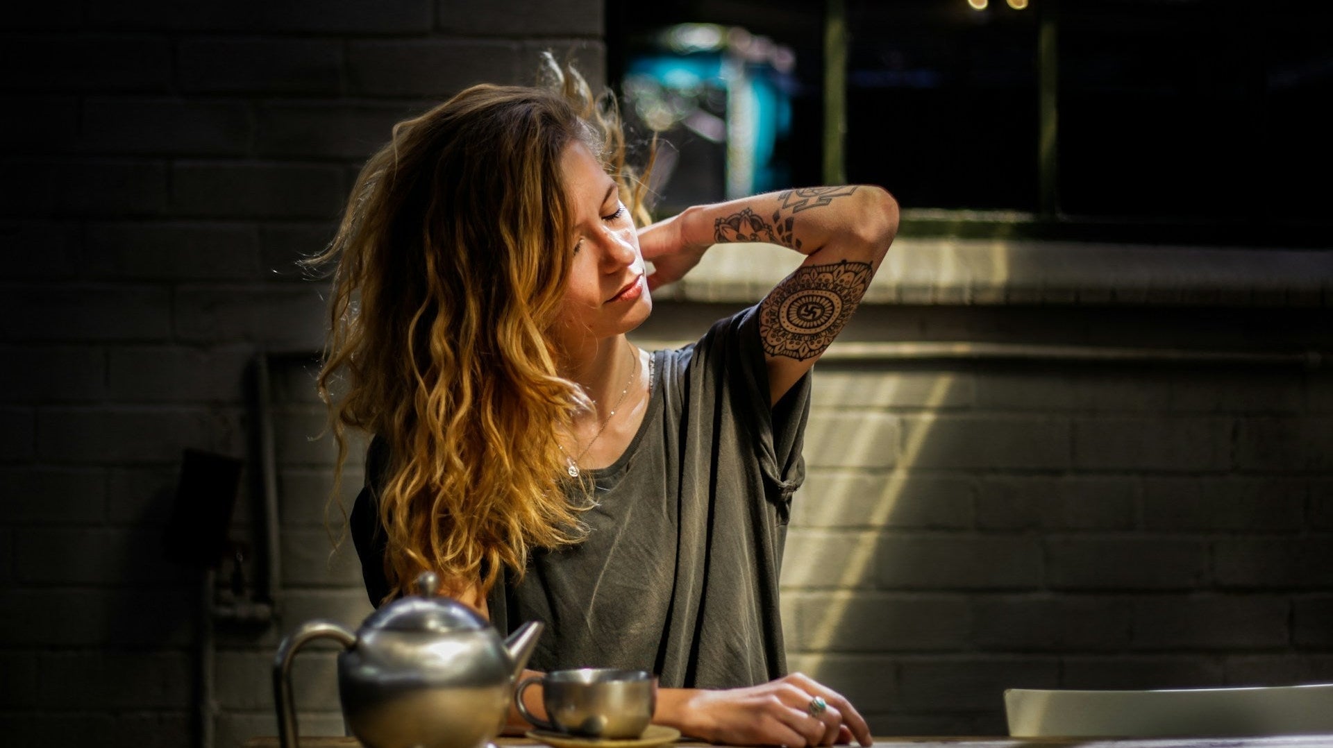 A woman stretching her neck at a table in a relaxed indoor setting, showing discomfort from sitting too long, illustrating how to avoid back pain while sitting for long hours.