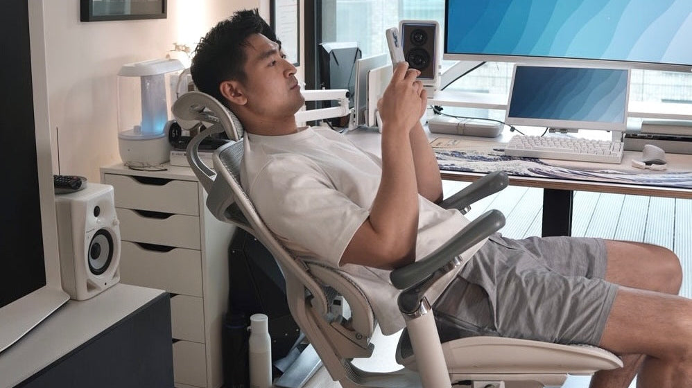 Man sitting on a high-end office chair with recline function in a stylish, tech-equipped home office setup.