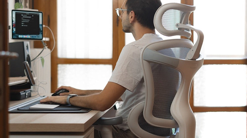 Man working at a desk with ergonomic chair and computer, related to tracking home office expenses.