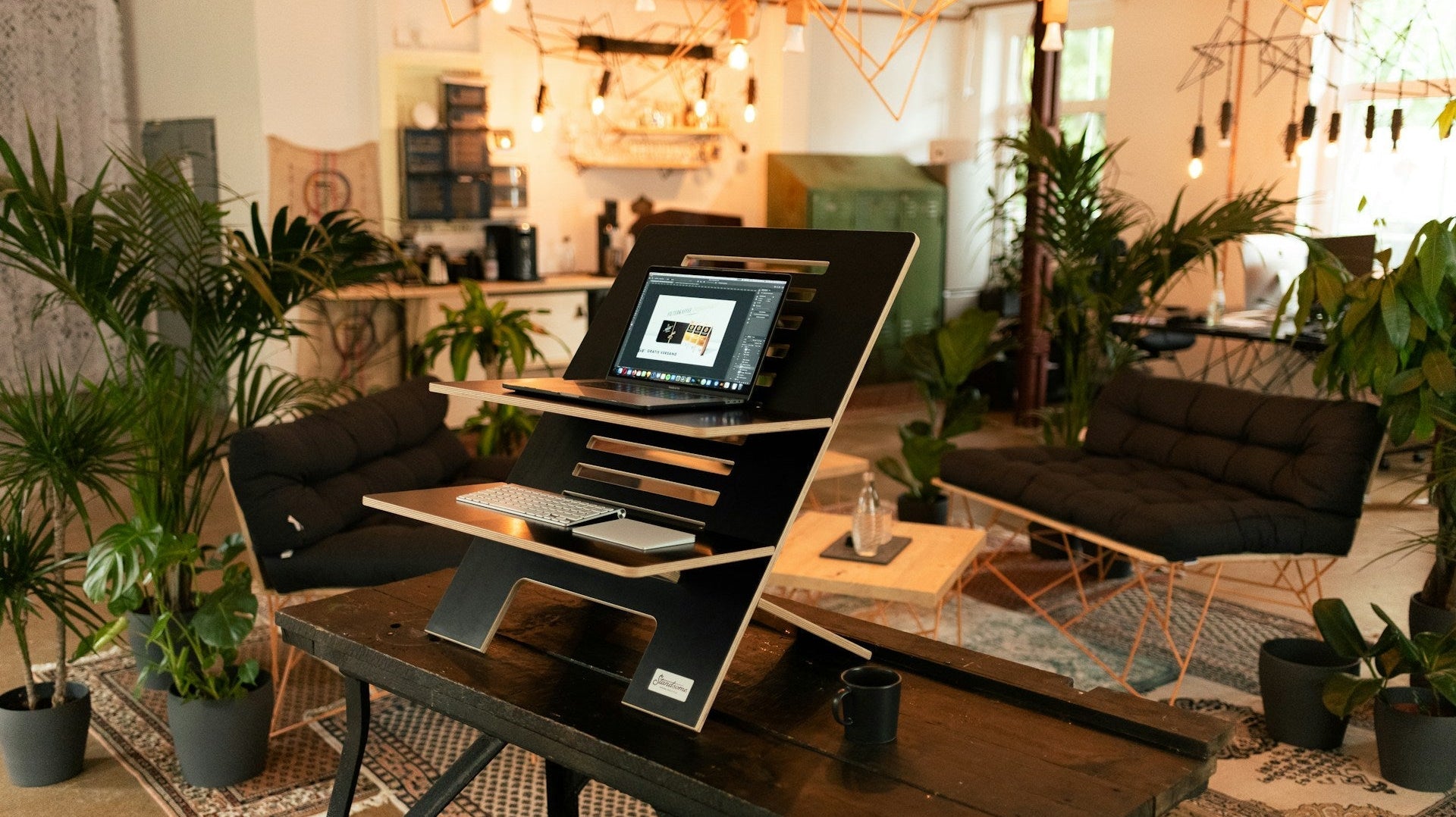 Modern home office furniture setup featuring a laptop stand, lush plants, and cosy seating in a stylish, inviting living space.