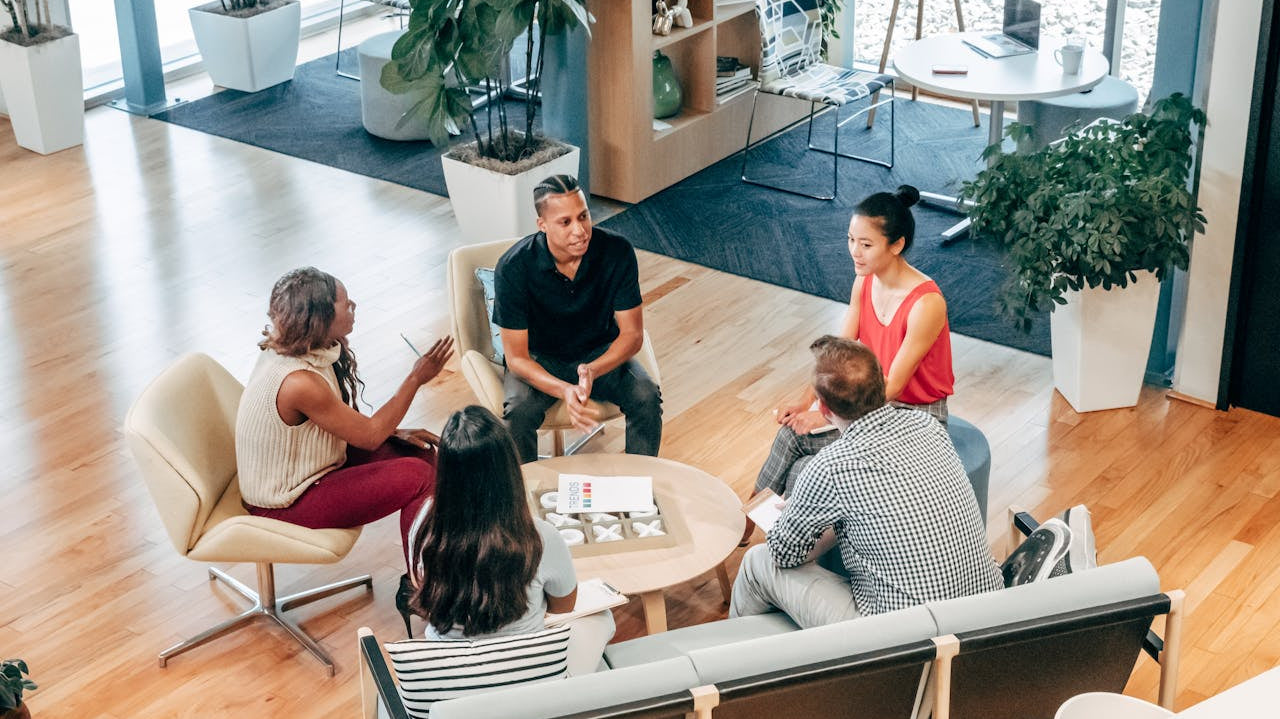 A diverse group discusses morning habits of highly productive people in a bright, modern office with plants and natural light.