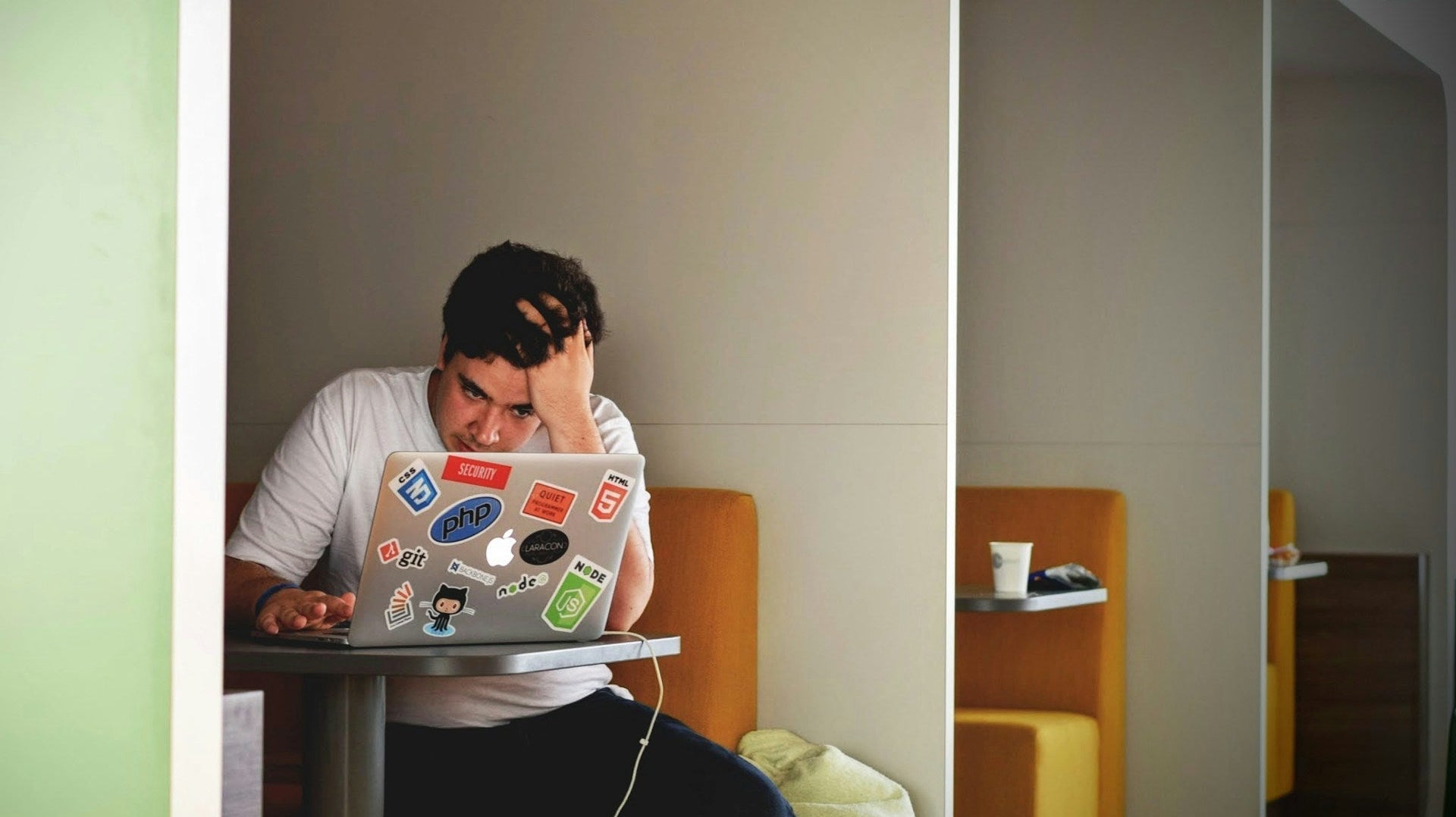 An exhausted man still working inside an office cafe, embodying workaholism in the remote work era. Image by Tim Gouw via www.unsplash.com