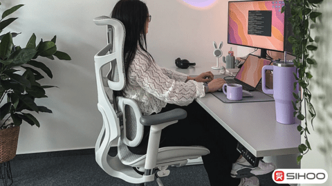 A woman sitting and working at her work-from-home setup table using an ergonomic office chair that helps prevent hunchback and supports proper posture.