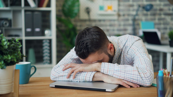 Man sitting at a desk with his head in his hands, showing stress and mental fatigue at work that needs ergonomic chair