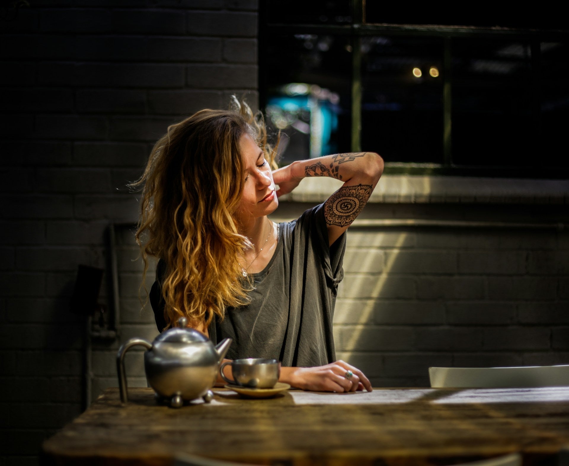 A woman stretching her neck at a table in a relaxed indoor setting, showing discomfort from sitting too long, illustrating how to avoid back pain while sitting for long hours.