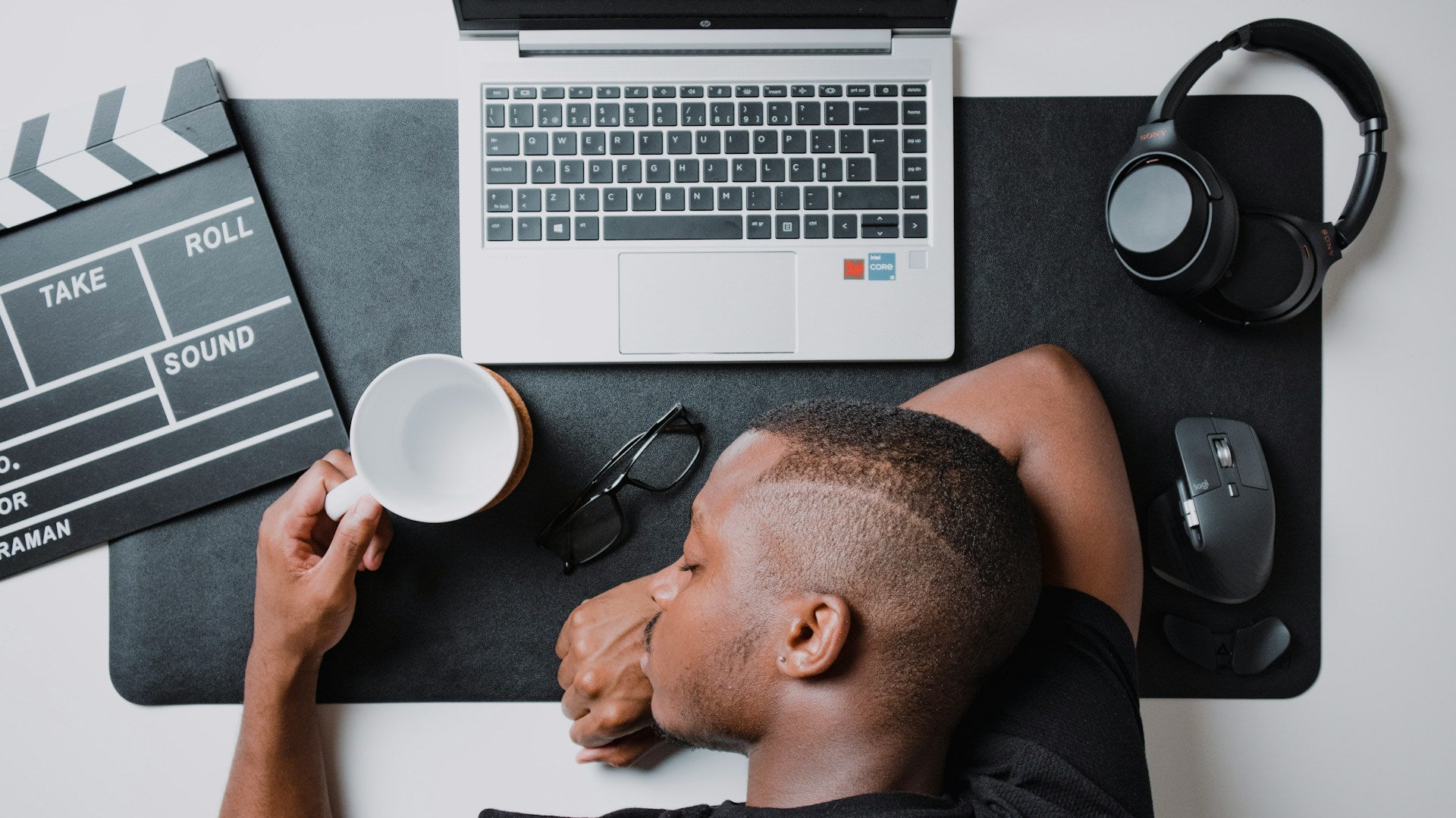 Man asleep at desk with laptop, coffee, and headphones, reflecting exhaustion and the question of how long does a burnout last in daily life. Image by Nubelson Fernandes via www.unsplash.com