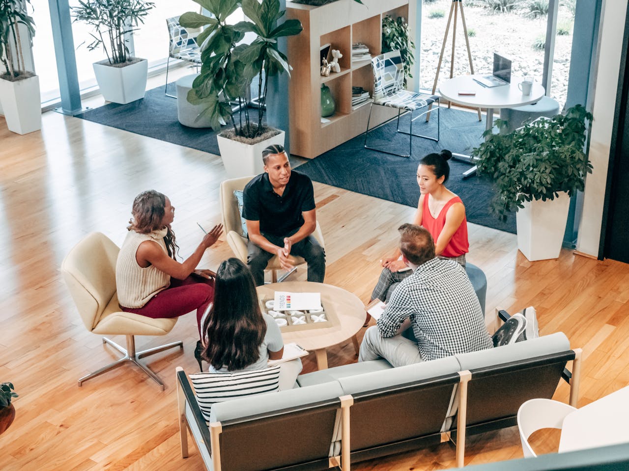 A diverse group discusses morning habits of highly productive people in a bright, modern office with plants and natural light.