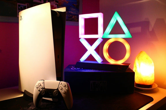 A row of gaming consoles placed on a table in dimly lit room, insipiring the question which gaming console should i buy. IMage by Roberto Vincenzo Minasi via www.unsplash.com