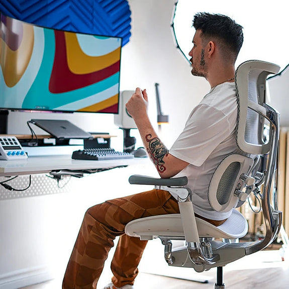 Man sitting on white ergonomic chair in Australia facing a computer monitor in a home office setup.