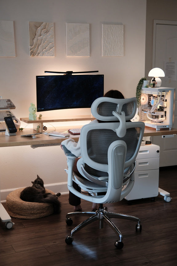 Woman in a work-from-home setup sitting on a white ergonomic chair with a cat under the table.