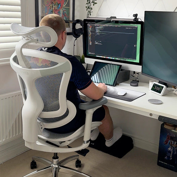 Man seated on white ergonomic chair in Australia looking at computer monitor in a modern home office workspace