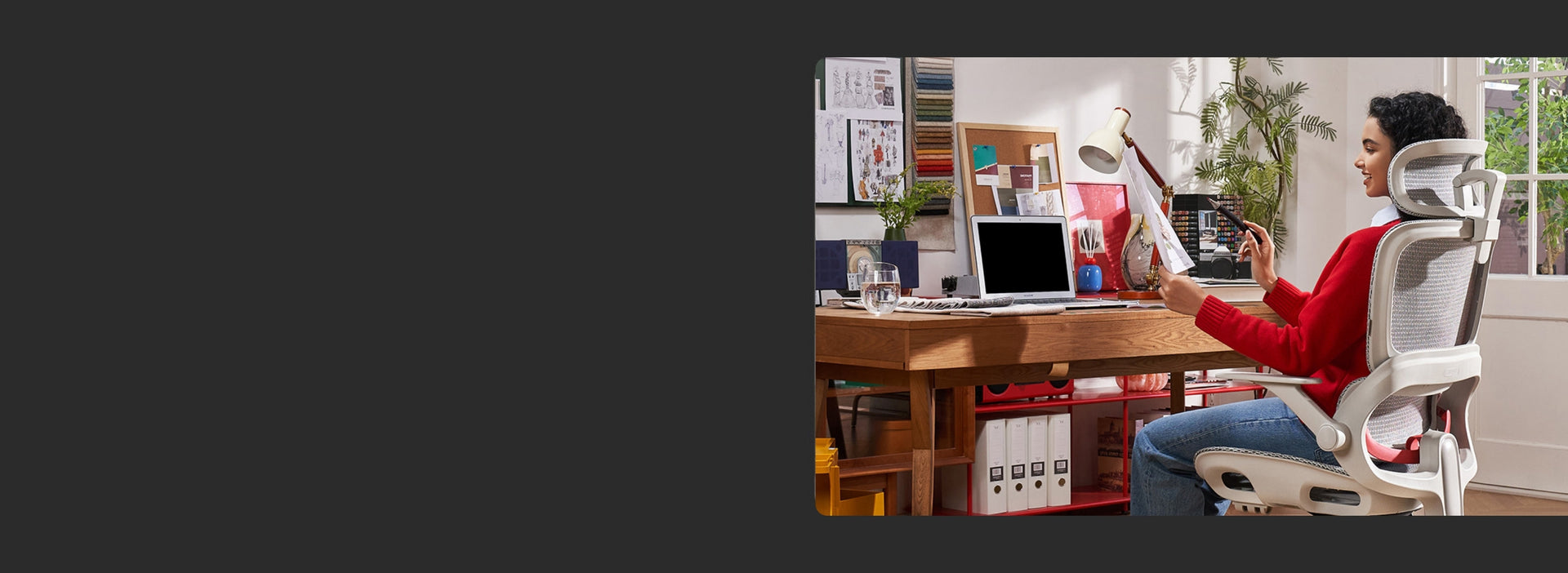 Banner image of a creative professional working on a laptop while seated on a white ergonomic chair in a colorful home office setup.