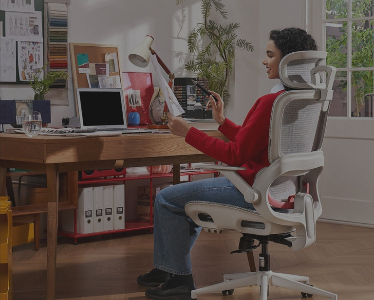 Creative professional working on a laptop while seated on a white ergonomic chair in a colorful home office setup.