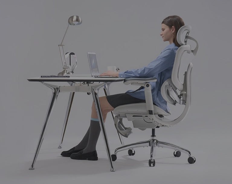 Woman wearing a blue top seated on a white ergonomic chair.